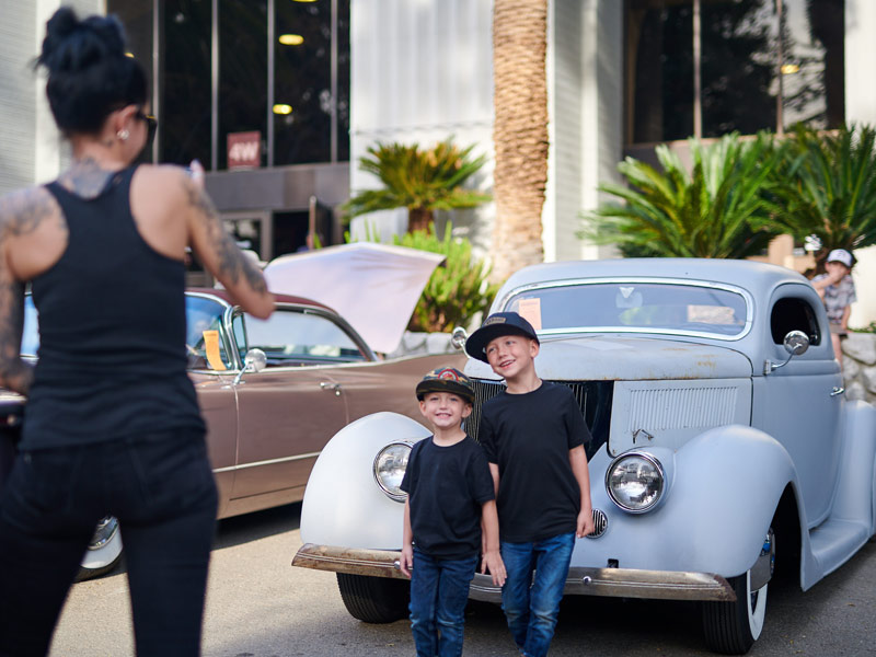 Mom taking photo of two boys in front of vintage car